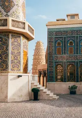 Intricately patterned mosaic buildings and traditional pigeon towers at Katara Cultural Village in Doha, with warm-toned tiles and detailed ornamentation.