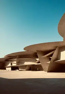 The National Museum of Qatar’s striking interlocking disc architecture under a clear blue sky, creating dramatic shadows across the open plaza.